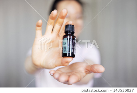 Woman holding essential oil bottle labeled Balance, showcasing natural wellness concept, with soft background emphasizing tranquility and holistic health benefits Woman holding essential oil bottle labeled Balance, showcasing natural wellness concept, with soft background emphasizing tranquility and holistic health benefits 143530027