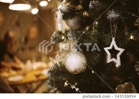 Christmas tree adorned with festive ornaments, including a star and glass bauble, creating a warm holiday atmosphere in a cozy indoor setting with soft lighting Christmas tree adorned with festive ornaments, including a star and glass bauble, creating a warm holiday atmosphere in a cozy indoor setting with soft lighting 143530054