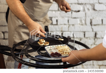 Cooking grilled cheese. Chef hands holding tongs and putting pieces of cheese on plate. Waiter holds tray with soft traditional Cypriot pickled haloumi and jam. Cooking grilled cheese. Chef hands holding tongs and putting pieces of cheese on plate. Waiter holds tray with soft traditional Cypriot pickled haloumi and jam. 143530090
