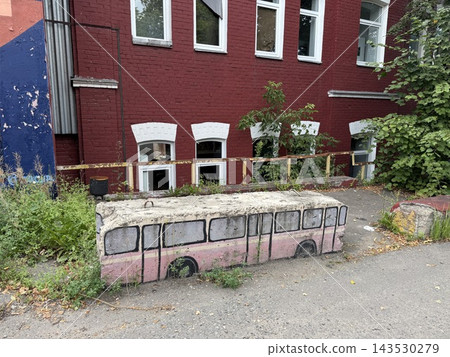 Abandoned pink bus bench beside overgrown courtyard and red brick building with windows and graffiti wall Abandoned pink bus bench beside overgrown courtyard and red brick building with windows and graffiti wall 143530279