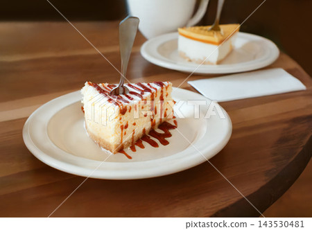 Slice of delicious cheesecake topped with caramel sauce and coconut flakes on a white plate with a fork. Desserts and coffee cup served on wooden table in cafe. Slice of delicious cheesecake topped with caramel sauce and coconut flakes on a white plate with a fork. Desserts and coffee cup served on wooden table in cafe. 143530481