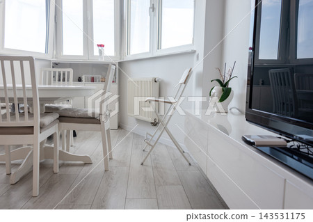 Bright minimalist dining and living area with white furniture and a potted plant by the window. Interior design, minimalism, home lifestyle, calm, simplicity, cozy morning. Bright minimalist dining and living area with white furniture and a potted plant by the window. Interior design, minimalism, home lifestyle, calm, simplicity, cozy morning. 143531175
