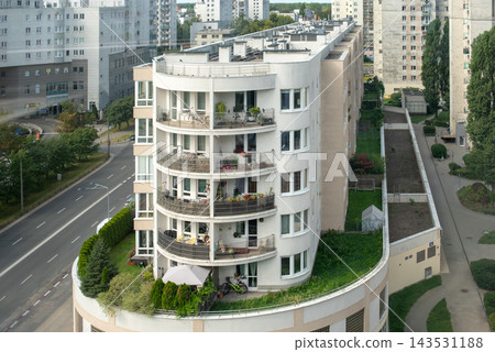 Residents use balconies and a rooftop garden in a curved urban apartment building. Urban living, community, sustainability, balcony garden, family life, modern housing. 143531188
