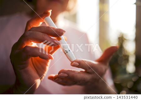 Elderly woman with light skin using a diabetes pen to check blood sugar levels, soft natural light illuminating her hands and the pen in a home setting Elderly woman with light skin using a diabetes pen to check blood sugar levels, soft natural light illuminating her hands and the pen in a home setting 143531440