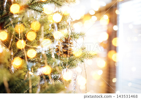 Close-up of a decorated Christmas tree featuring a pine cone ornament and warm glowing lights creating a festive atmosphere in a cozy indoor setting Close-up of a decorated Christmas tree featuring a pine cone ornament and warm glowing lights creating a festive atmosphere in a cozy indoor setting 143531468
