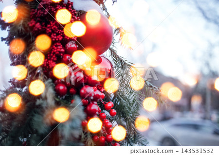 Close-up of festive Christmas decorations featuring red ornaments and berries with blurred warm lights in the background, creating a holiday atmosphere Close-up of festive Christmas decorations featuring red ornaments and berries with blurred warm lights in the background, creating a holiday atmosphere 143531532