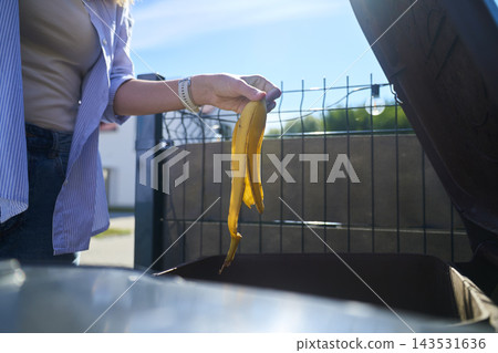 Woman throwing banana peel into open brown waste bin outside her home Woman throwing banana peel into open brown waste bin outside her home 143531636