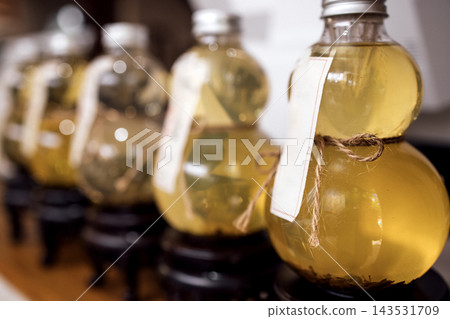Decorative glass bottles filled with herbal infusion displayed on wooden stand, featuring labels and twine accents, arranged in a row for aesthetic presentation Decorative glass bottles filled with herbal infusion displayed on wooden stand, featuring labels and twine accents, arranged in a row for aesthetic presentation 143531709