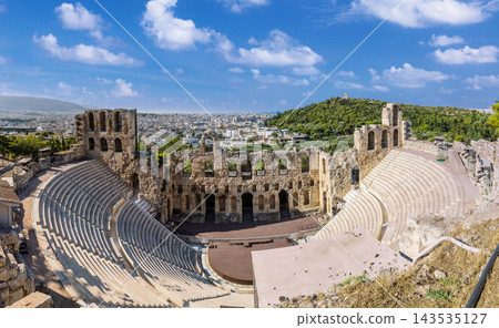 Odeon of Herodes Atticus ancient theater ruins with Athens cityscape in background under blue sky 143535127