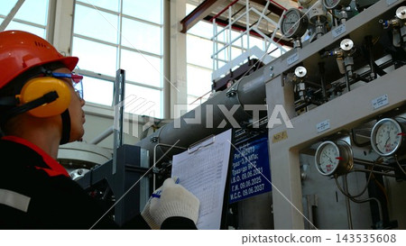 Protective gear worker fills inspection form near heavy industrial equipment, using clipboard and pen with focused expression. Maintenance worker faces pressure gauges and piping in spacious factory Protective gear worker fills inspection form near heavy industrial equipment, using clipboard and pen with focused expression. Maintenance worker faces pressure gauges and piping in spacious factory 143535608