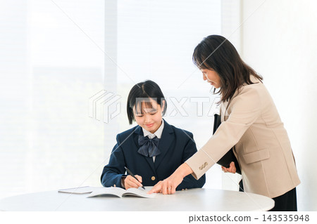 A high school girl in uniform receives instruction from a female tutor. A one-on-one study session between teacher and student. A high school girl in uniform receives instruction from a female tutor. A one-on-one study session between teacher and student. 143535948