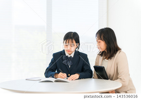A high school girl in uniform diligently studies for her entrance exams, watched over by her female tutor. An image of individual tutoring and exam preparation. A high school girl in uniform diligently studies for her entrance exams, watched over by her female tutor. An image of individual tutoring and exam preparation. 143536016