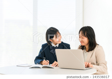 A high school girl in uniform receives individual tutoring from a female instructor using a computer. The image evokes the idea of a smiling student studying for entrance exams. A high school girl in uniform receives individual tutoring from a female instructor using a computer. The image evokes the idea of a smiling student studying for entrance exams. 143536017