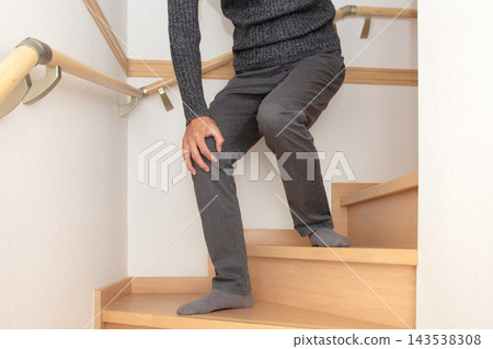 一個人扶著樓梯半腰的扶手，痛苦地摀住膝蓋。 143538308