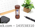 An hourglass, a calendar, and a smartphone are placed on the desk. 143538310