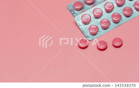 Pink round tablets in silver blister packs beside three loose pills on a pink surface, oral pharmaceutical products with clear plastic pockets for women's health and vitamin supplement communication. 143538370