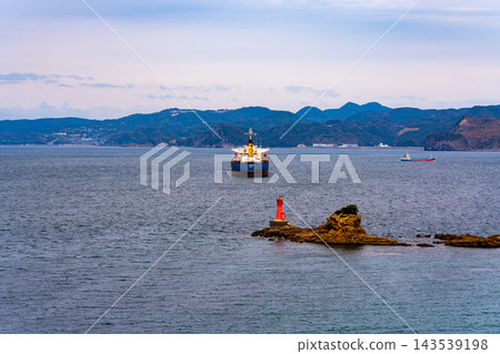 A cargo ship and a lighthouse floating in a calm bay A cargo ship and a lighthouse floating in a calm bay 143539198