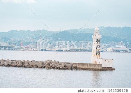 防波堤上的燈塔，背景是山脈和城鎮。 143539556