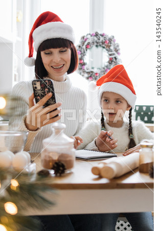 A mother and daughter wearing Santa hats are on a video call during Christmas preparations 143540245