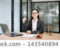 Asian female lawyer in a suit and glasses sitting at her modern office desk. Professional attorney providing trusted legal advice Asian female lawyer in a suit and glasses sitting at her modern office desk. Professional attorney providing trusted legal advice 143540894