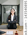 Asian female lawyer in a suit holding a contract in her office. Confident attorney standing by a desk Asian female lawyer in a suit holding a contract in her office. Confident attorney standing by a desk 143540895