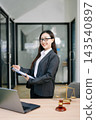 Asian female lawyer in a suit holding a contract in her office. Confident attorney standing by a desk Asian female lawyer in a suit holding a contract in her office. Confident attorney standing by a desk 143540897