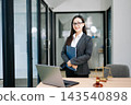 Asian female lawyer in a suit holding a contract in her office. Confident attorney standing by a desk Asian female lawyer in a suit holding a contract in her office. Confident attorney standing by a desk 143540898