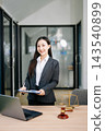 Asian female lawyer in a suit holding a contract in her office. Confident attorney standing by a desk Asian female lawyer in a suit holding a contract in her office. Confident attorney standing by a desk 143540899