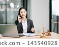 Asian female lawyer talking on a smartphone at her modern office desk. Confident attorney giving legal advice near a laptop, gavel Asian female lawyer talking on a smartphone at her modern office desk. Confident attorney giving legal advice near a laptop, gavel 143540928