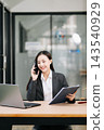 Asian female lawyer talking on a smartphone at her modern office desk. Confident attorney giving legal advice near a laptop, gavel Asian female lawyer talking on a smartphone at her modern office desk. Confident attorney giving legal advice near a laptop, gavel 143540929