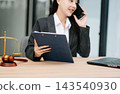 Asian female lawyer talking on a smartphone at her modern office desk. Confident attorney giving legal advice near a laptop, gavel Asian female lawyer talking on a smartphone at her modern office desk. Confident attorney giving legal advice near a laptop, gavel 143540930