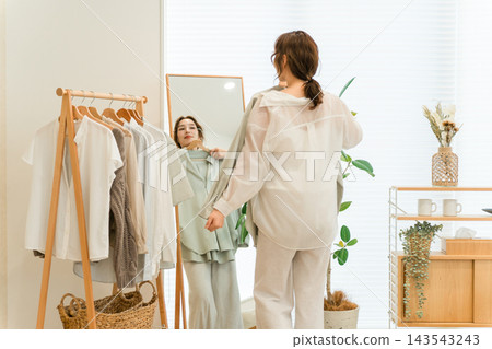 一位女士在家裡的客廳裡，對著鏡子試穿衣服。她享受著搭配服裝和挑選衣服的樂趣。 143543243