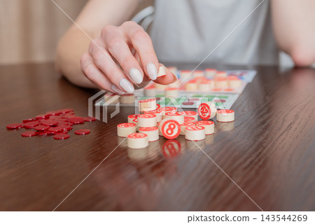 Person's hand lifting a wooden number token from a pile on a dark table during a casual board game, close up capturing leisure, strategy and friendly competition Person's hand lifting a wooden number token from a pile on a dark table during a casual board game, close up capturing leisure, strategy and friendly competition 143544269