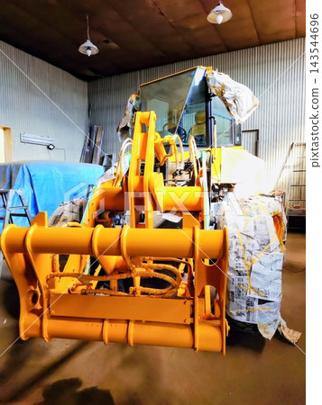 Attachments of heavy machinery partially protected with protective sheets in preparation for full painting. Attachments of heavy machinery partially protected with protective sheets in preparation for full painting. 143544696
