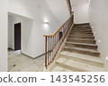 A modern staircase in a well-lit hallway. The stairs are made of stone with a wooden railing. The walls are painted white, creating a clean and minimalist look. 143545256