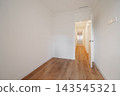 A bright, empty hallway with white walls and wooden flooring. The space is well-lit, leading to an open area in the background. 143545321