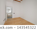 A modern, empty room with white walls and wooden flooring. A doorway leads to a bathroom area. Natural light enters through a window. 143545322