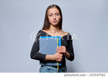 Young female student holding notebook in studio portrait Young female student holding notebook in studio portrait 143547562
