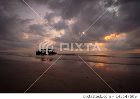 Tractor Pulls Fishing Boat on a tranquil tropical beach at sunset, under a dramatic sky filled with warm orange and purple clouds. Calm waves reflect the vibrant colors. Tractor Pulls Fishing Boat on a tranquil tropical beach at sunset, under a dramatic sky filled with warm orange and purple clouds. Calm waves reflect the vibrant colors. 143547609