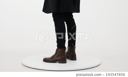 Person wearing modern brown leather boots with black pants on a white platform, presenting current fashion and footwear trends Person wearing modern brown leather boots with black pants on a white platform, presenting current fashion and footwear trends 143547850
