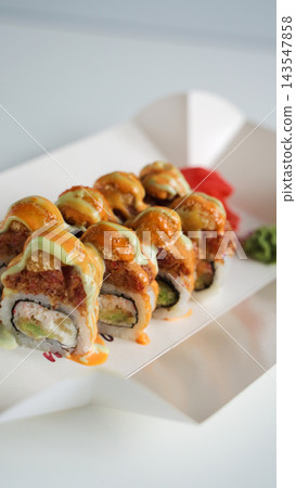 Spicy fried sushi rolls with orange and green sauces, served with pickled ginger and wasabi in white takeaway box Spicy fried sushi rolls with orange and green sauces, served with pickled ginger and wasabi in white takeaway box 143547858