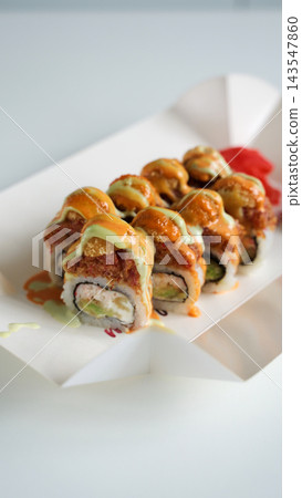 Spicy fried salmon maki rolls with avocado and cream cheese, topped with sauce and ginger, in a takeaway box Spicy fried salmon maki rolls with avocado and cream cheese, topped with sauce and ginger, in a takeaway box 143547860
