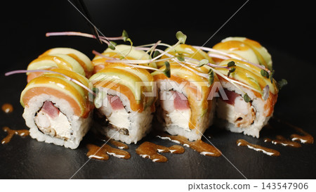 Uramaki sushi rolls on a dark background, chef adding sauce and microgreens, gourmet Japanese food Uramaki sushi rolls on a dark background, chef adding sauce and microgreens, gourmet Japanese food 143547906