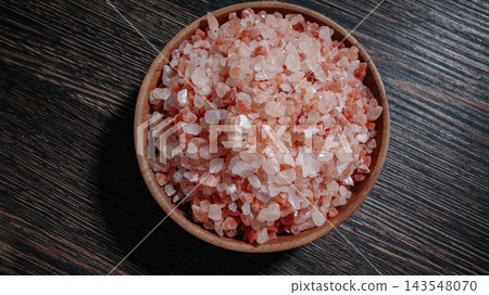 Wooden bowl filled with pink Himalayan salt crystals on dark wooden table, natural mineral seasoning for healthy cooking and spa concepts. Wooden bowl filled with pink Himalayan salt crystals on dark wooden table, natural mineral seasoning for healthy cooking and spa concepts. 143548070