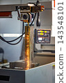 Wire EDM cutting of metal workpiece with sparks in industrial machine. 143548101