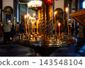 Golden Orthodox church candle holder with burning candles and worshippers in soft bokeh background. 143548104