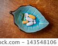 Assorted pills in a turquoise leaf shaped ceramic dish on a wooden table. 143548106