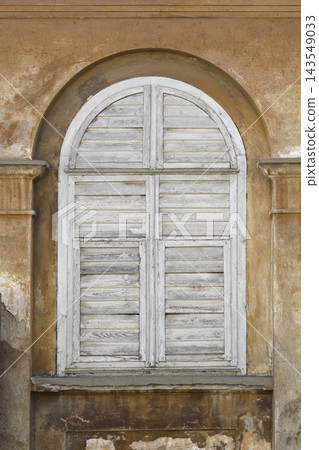 Old arched window with closed wooden shutters on a weathered facade Old arched window with closed wooden shutters on a weathered facade 143549033