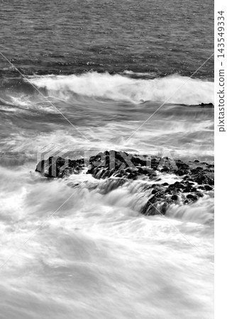 Black and white, long exposure shot of the rocky shore and Sagami Bay with whitecaps rising in strong winds, as seen from the Enoshima Shonan Great Breakwater. Black and white, long exposure shot of the rocky shore and Sagami Bay with whitecaps rising in strong winds, as seen from the Enoshima Shonan Great Breakwater. 143549334