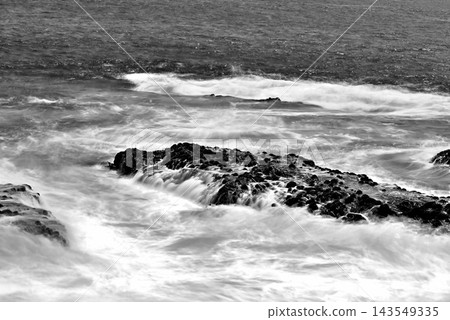 從江之島湘南大防波堤上拍攝的黑白長曝光照片,展現了岩石海岸和相模灣在強風中激起的白色浪花。 從江之島湘南大防波堤上拍攝的黑白長曝光照片,展現了岩石海岸和相模灣在強風中激起的白色浪花。 143549335